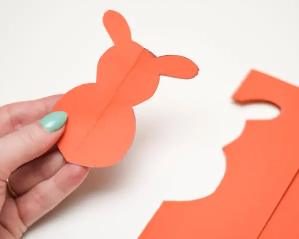 En hand håller en orange pappersfigur av en påskhare.