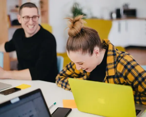 Zwei lachende Kollegen am Schreibtisch mit Laptops. Ein bezahltes Auslandspraktikum kann so Spaß machen!