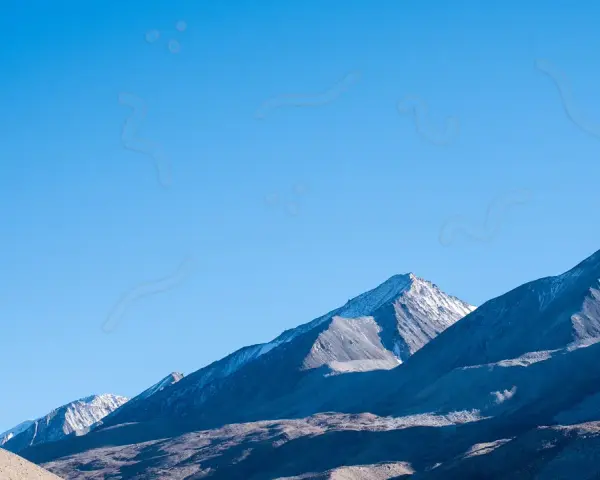 Sullo sfondo di montagne innevate, un cielo azzurro limpido è punteggiato da forme sinchisi scintillante, come piccoli puntini e curve sinuose.