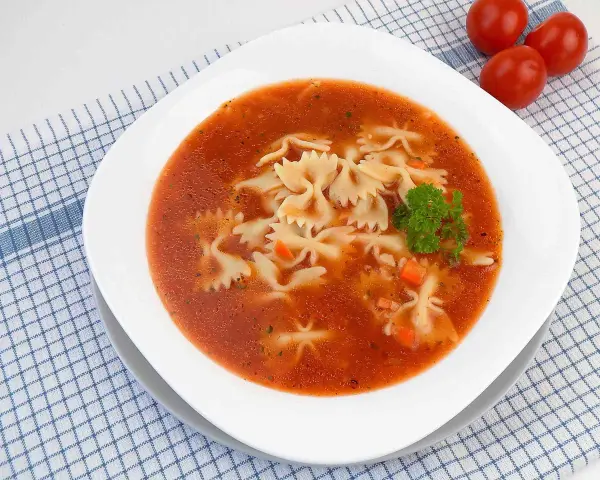 Zupa pomidorowa z makaronem farfalle, marchewką i natką pietruszki na kratkowanym obrusie.