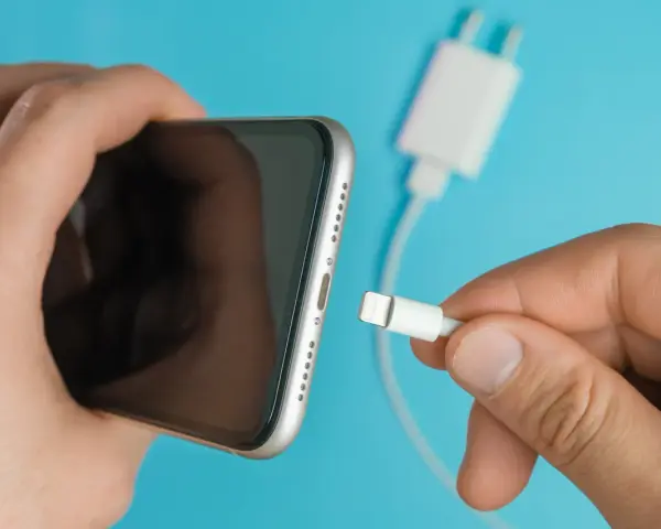 En hand håller en iPhone och en laddkabel. Var försiktig med vatten i ladduttaget på din iPhone.