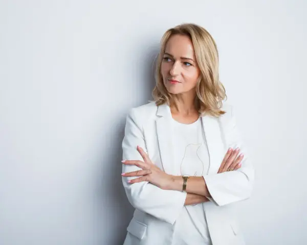 Elegancka kobieta w białej marynarce, z rękami skrzyżowanymi na piersi. Idealne zdjęcie do CV, podkreślające profesjonalizm i pewność siebie.