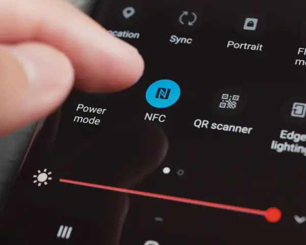 En finger pekar på NFC-ikonen på en mobilskärm. Snabbinställningar visas, inklusive "Power mode" och "QR scanner".