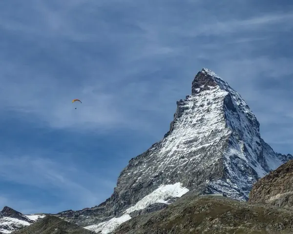 Widok na ośnieżony szczyt Matterhornu, z paralotnią szybującą na błękitnym niebie. To jak wejście na Mont Blanc dla odważnych.