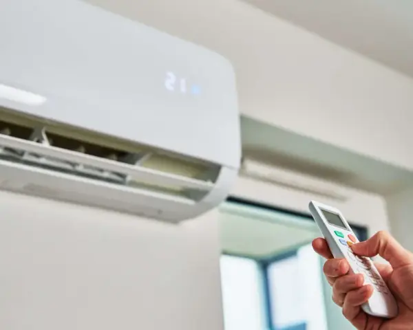 Mano operando el control remoto de un aire acondicionado, indicando la temperatura de 21 grados. Es hora del mantenimiento.