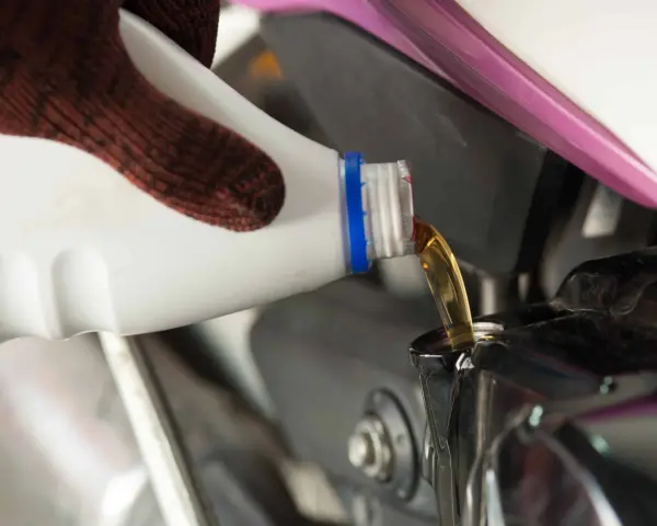 Rękawica nalewa nowy olej do silnika motocykla podczas wymiany oleju.