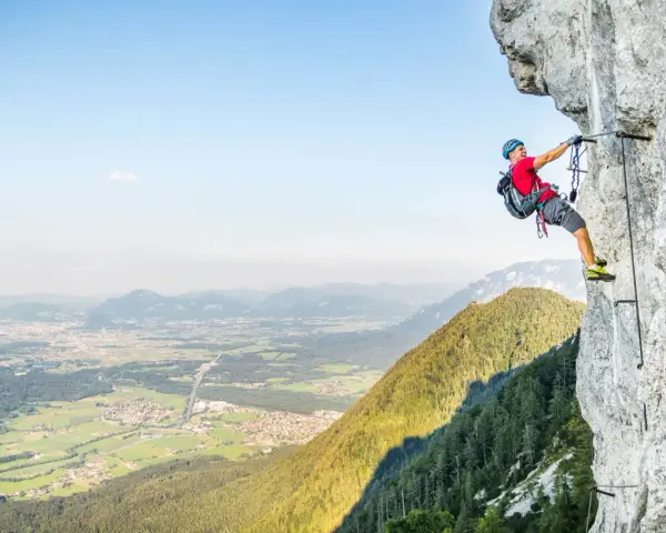 Ein Mann klettert gesichert an einem Stahlseil einen Felsgrat entlang. Ein Abenteuer auf einem der vielen Klettersteige Deutschlands.