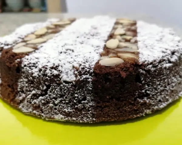 Torta caprese ricetta originale napoletana, soffice e scura, cosparsa di zucchero a velo e mandorle a lamelle.
