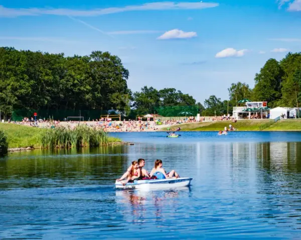Rodzina na rowerku wodnym na jeziorze, plaża pełna ludzi, las i budynki w tle. Idealne miejsce gdzie nad wodę Dolny Śląsk.
