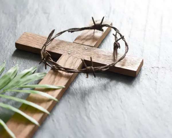 Holzkreuz mit Dornenkrone und Palmblatt. Christen fasten Regeln, um sich auf Ostern vorzubereiten.