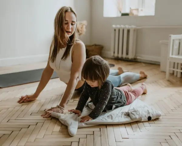 Mama i dziecko ćwiczą jogę. Maluch leży na poduszce w kształcie wieloryba, a mama w pozycji kobry. To świetne ćwiczenia relaksacyjne dla dzieci.