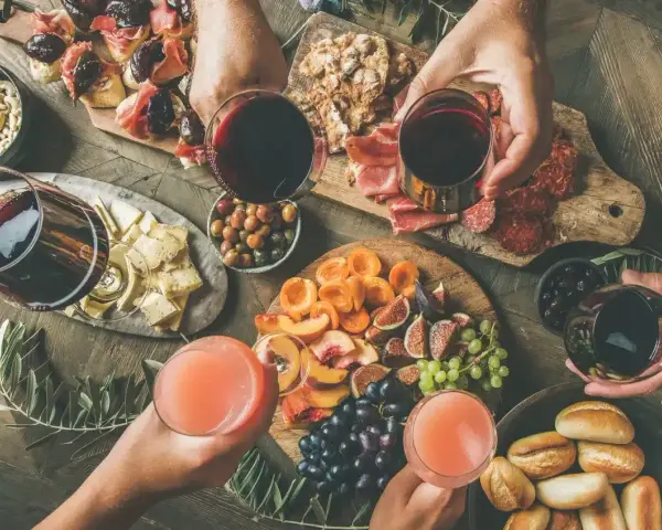Stół z przekąskami: wędliny, sery, owoce, pieczywo i napoje.
