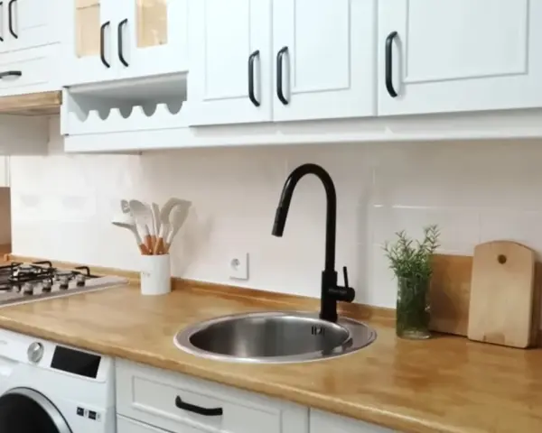 Cocina renovada: gabinetes blancos, encimera de madera y grifo negro. ¡Un ejemplo de cómo pintar muebles de melamina para darles nueva vida!