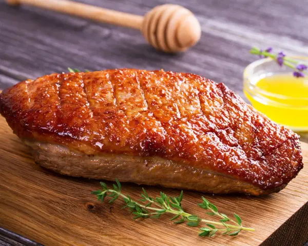 Un magret de canard au barbecue, la peau dorée et croustillante, prêt à être dégusté avec une touche de miel et de thym.