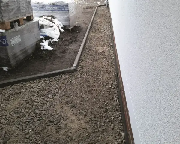 Stos **wapien** w budowie ścieżki wokół domu. Materiały budowlane leżą na ziemi, częściowo przykryte śniegiem.