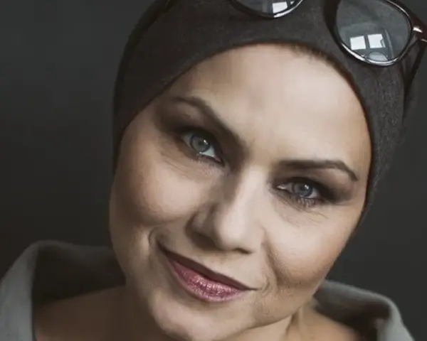 Sylwia Janowicz-Dobrowolska w szarej opasce i okularach na głowie, z wyrazistym makijażem oczu i błyszczącymi ustami.