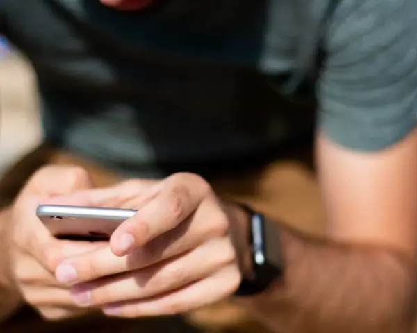 Mężczyzna trzyma smartfon, a na jego nadgarstku widać smartwatch. Właśnie sprawdza, jak sparować zegarek z telefonem.