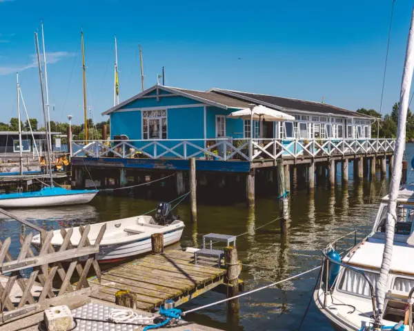 Blaues Haus am Wasser mit Booten, ein idyllisches Motiv für Schlei Ausflugsziele.