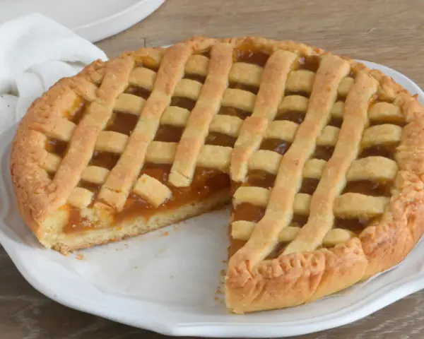 Crostata con marmellata, un classico della crostata ricetta tradizionale, servita su un piatto bianco con un tovagliolo di lino.