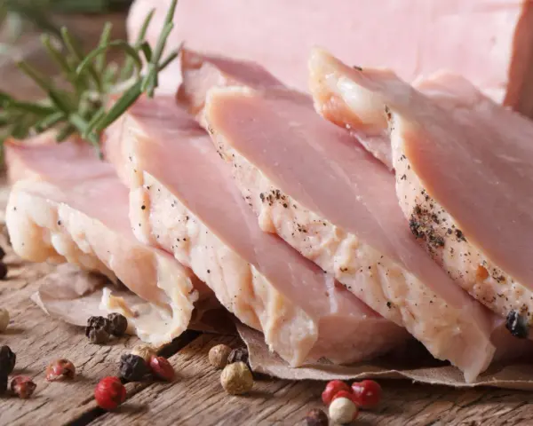 Super delikatny i soczysty schab gotowany, pokrojony w plastry, z gałązką rozmarynu i ziarnami pieprzu.