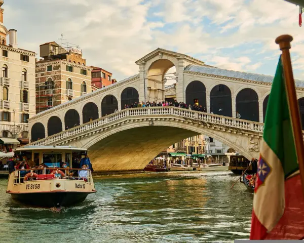 Traghetto della linea 2 di Venezia naviga sul Canal Grande sotto il Ponte di Rialto, con gondole e edifici storici sullo sfondo.