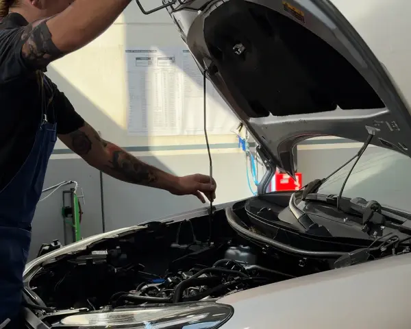 Meccanico con tatuaggi controlla il motore. Capire la differenza tra tagliando e revisione è fondamentale per la manutenzione dell'auto.