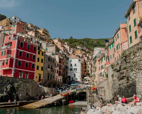 Colorful buildings cling to a hillside overlooking a harbor, a picturesque scene after a train from Bologna to Cinque Terre.