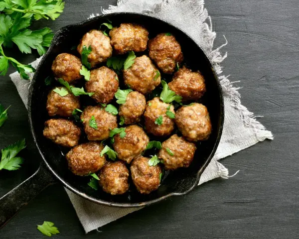 Polpette al forno dorate e succulente, guarnite con prezzemolo fresco, in una padella di ghisa su sfondo scuro.
