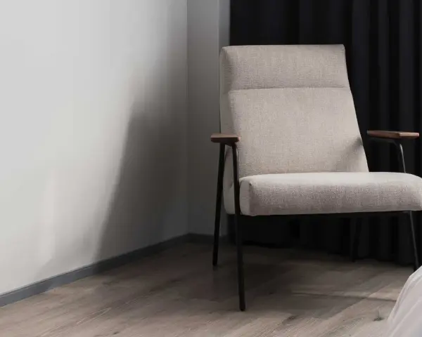Fauteuil moderne avec un élégant tissu assise chaise, pieds fins et accoudoirs en bois. Il est placé près d'un mur blanc et de rideaux sombres.