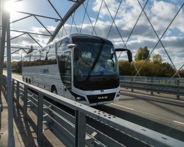Biały autokar PKS NOVA jedzie przez most, pokonując trasę Warszawa-Augustów.