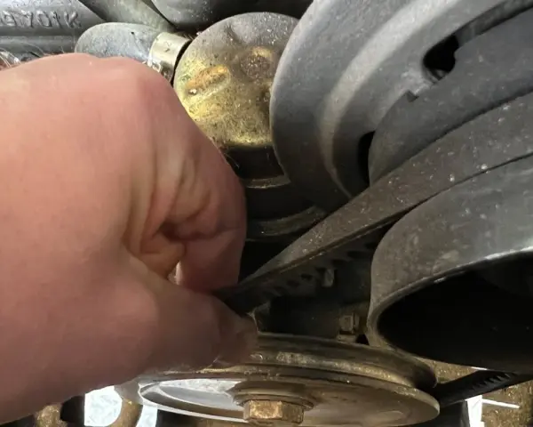 Hand prüft Keilriemen, der beim Anfahren quietscht. Der Riemen läuft über mehrere Riemenscheiben im Motorraum.