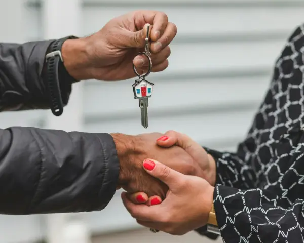 Une main tend une clé de maison, l'autre la saisit. Une poignée de main scelle un accord, peut-être une solution quand un indivisaire ne paye pas.