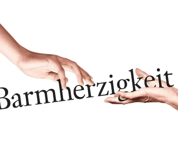 Zwei Hände berühren das Wort "Barmherzigkeit". Eine Hand reicht es der anderen, ein Symbol für die Werke der Barmherzigkeit.