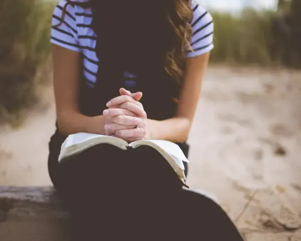 Kobieta z dłońmi złożonymi nad otwartą Biblią. To jej modlitwa o dobry dzień w pracy.