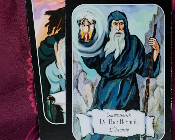 El tarot del mundo ermitaño: un sabio anciano con barba blanca ilumina el camino con una linterna, guiando en la introspección.
