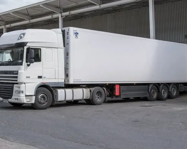 Biała naczepa DAF XF z chłodnią, gotowa do transportu. Obok stoi kolejna ciężarówka, tworząc zgrany zespół pojazdów.