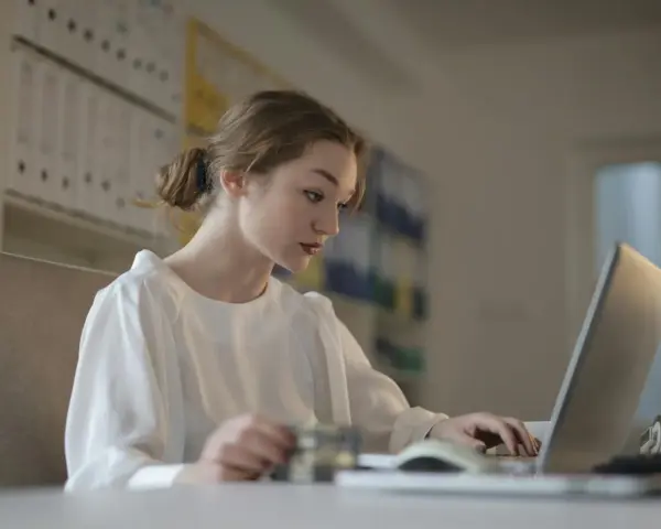 Młoda kobieta uczy się, jak zostać księgowym bez studiów, korzystając z laptopa i karty.