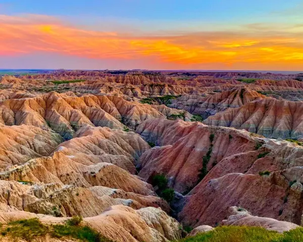 Un paisaje desértico con formaciones rocosas erosionadas, **las carcavas**, bajo un cielo anaranjado y azul al atardecer.