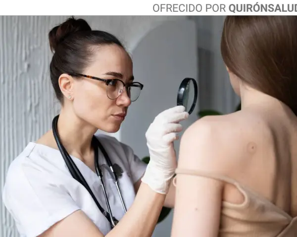 Dermatóloga examina lunares en la espalda de una paciente con lupa.