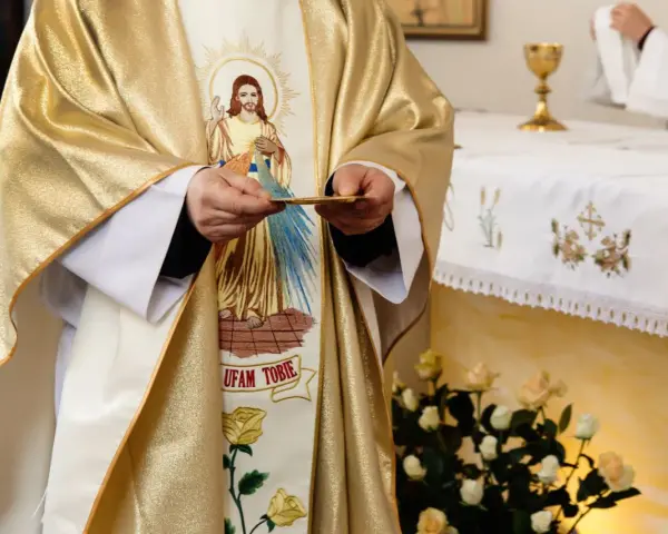 Kapłan w złotej szacie z wizerunkiem Jezusa trzyma hostię. Czy dzisiaj trzeba iść do kościoła?