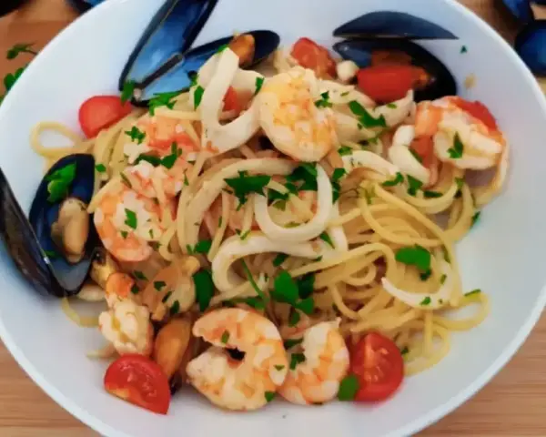 Pyszne linguini z krewetkami, kalmarami i małżami, ozdobione pomidorkami i natką pietruszki.