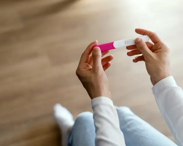 Dłonie trzymające test ciążowy, który wskazuje na 1 miesiąc ciąży.