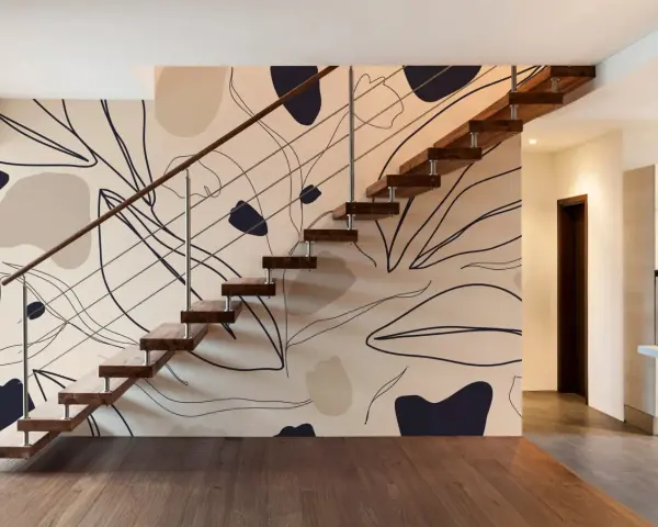 El papel pintado en las paredes de esta casa moderna presenta un diseño abstracto de hojas y formas orgánicas en tonos tierra, complementando la escalera flotante de madera.