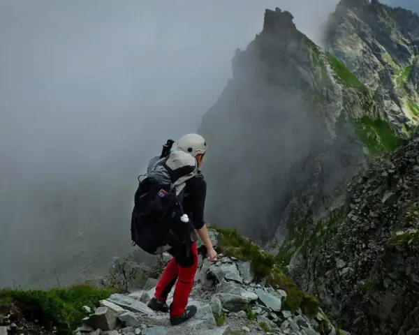 Osoba w kasku i z plecakiem przemierza skalisty szlak. Wspaniała przygoda w górach, prawdziwa turystyka piesza.