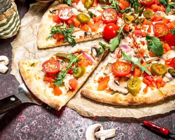 Kawałki pizzy z pomidorkami, jalapeno i rukolą na papierze do pieczenia.