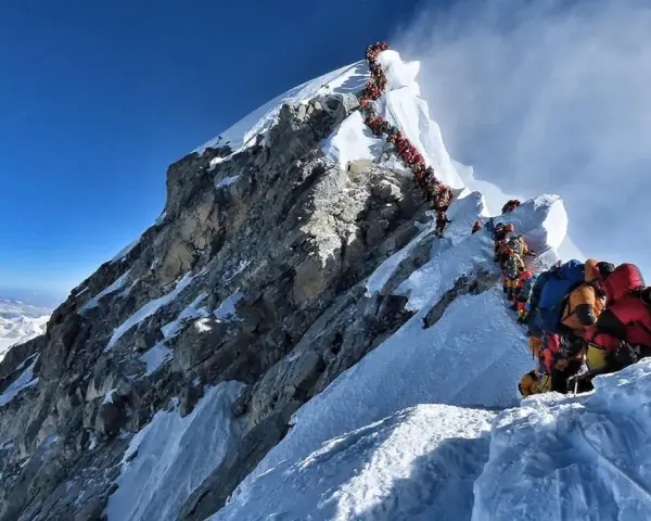 Kolejka ludzi wspinających się na najwyższą górę na świecie, Everest. Wspinacze w kolorowych kurtkach i z plecakami pokonują śnieżne zbocza.