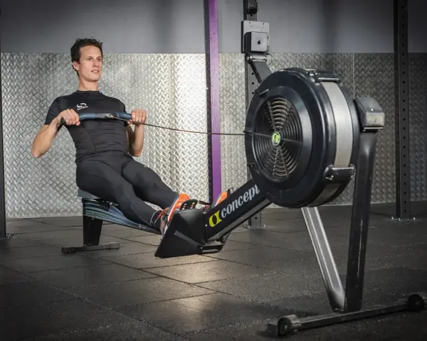 Un homme en tenue de sport effectue un exercice rameur dans une salle de sport.