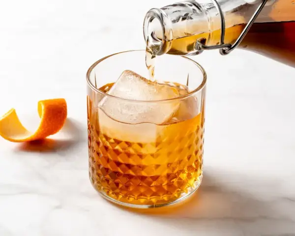 Amaretto co to? Bursztynowy likier z migdałów i moreli, nalewany do szklanki z lodem, z ozdobną skórką pomarańczy.