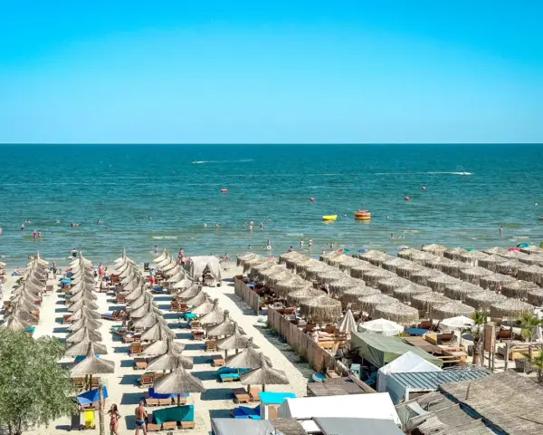 Słoneczna plaża w Rumunii, pełna leżaków i parasoli. Ludzie kąpią się w morzu, idealne miejsce na wakacje.