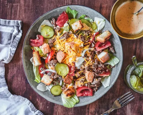 Ein Big Mac Salat mit Hackfleisch, Käse, Tomaten, Gurken und Croutons. Dazu eine cremige Sauce und eingelegte Gurken.